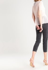 Světle růžový průhledný top s plissé pasem, kombinovaný s tmavě šedými zkrácenými džíny a nahými vysokými podpatky. Hladká textura a poloprůhledná látka.