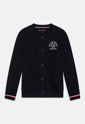 Sort cardigan med knapper og lange ærmer, hvide og røde striber på manchetterne samt "Hilfiger New York"-logo på venstre bryst.