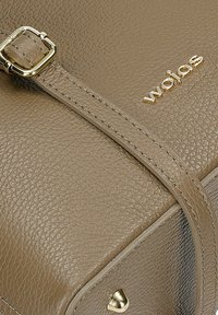 Lederhandtasche in Taubengrau mit einer strukturierten Oberfläche, ausgestattet mit einer goldfarbenen Schnalle und dem in Gold eingeprägten Markennamen "wojas".