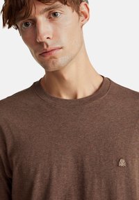 Maglietta a maniche lunghe marrone realizzata in tessuto morbido, con scollo rotondo e un piccolo logo ricamato sul lato sinistro del petto.