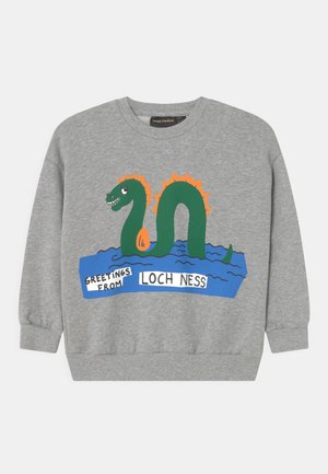 Grauer Pullover mit einer bunten Grafik eines Loch-Ness-Monsters, das aus blauem Wasser auftaucht, und dem Text "Grüße vom Loch Ness."