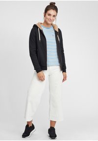 Black hoodie with tan sherpa lining, blue striped t-shirt, white wide-leg pants, and black sneakers. Simple design and casual fit.