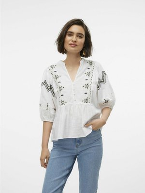 Hvid bluse med sorte broderede mønstre, en V-halsudskæring og puffærer, parret med lyseblå jeans. Struktureret stof med knapdetaljer.