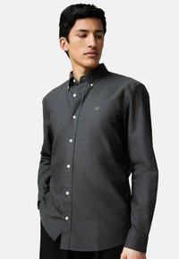 Camisa de botón gris oscuro con cuello, mangas largas y botones blancos. Bordado sutil en el pecho y textura de tejido suave.