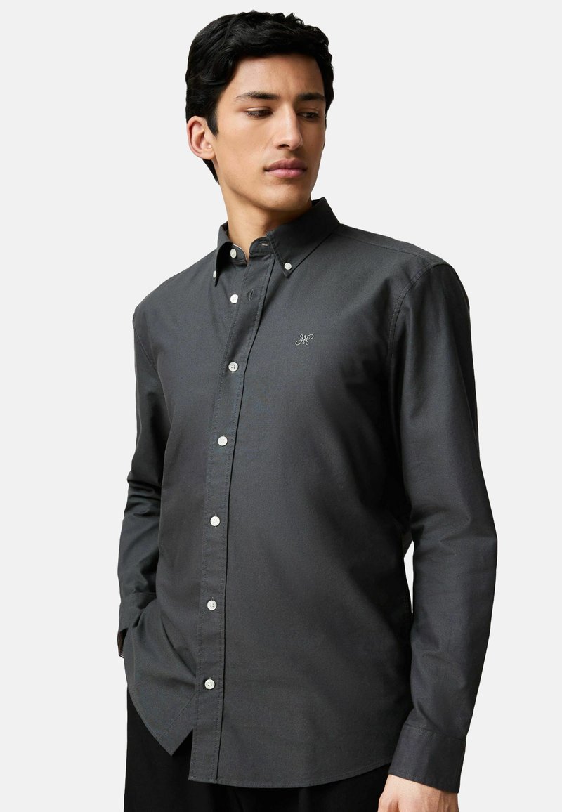 Camisa de botón gris oscuro con cuello, mangas largas y botones blancos. Bordado sutil en el pecho y textura de tejido suave.
