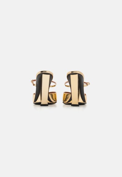 Sandalias de tacón alto en negro y dorado con un acabado pulido, que cuentan con un diseño anguloso, finas correas en el tobillo y un distintivo tacón geométrico.