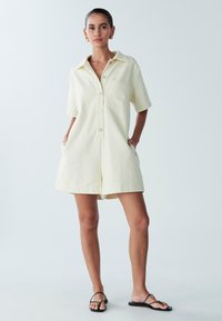 Korte mouwen, collared jumpsuit in zachtgele stof, met een borstzak, knoopsluiting en zijzakken. Eenvoudige, relaxte pasvorm.