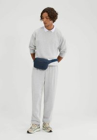 Sudadera gris y pantalones de chándal de tela suave, usados con una camisa blanca con cuello debajo. Riñonera azul oscuro con cremallera en la cintura.