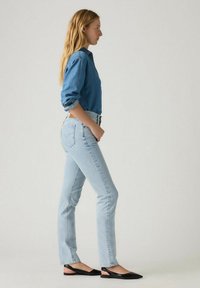 Jeans de mezclilla azul claro con un diseño de pierna recta, complementados por una blusa de mezclilla de botón. Unos zapatos planos de punta negra completan el atuendo.
