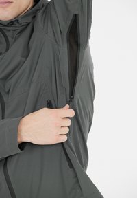 Grijze hoodie met een ritsventilatie; heeft een gladde, lichte stof met subtiele naaddetails en een mesh voering zichtbaar binnen de opening.