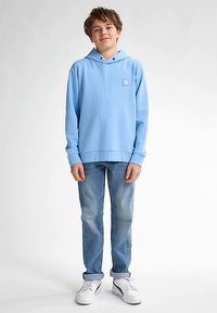 Felpa con cappuccio azzurro chiaro con toppa logo frontale, abbinata a jeans in denim lavaggio medio e sneakers bianche.