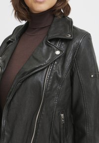 Black leather motorcycle jacket with silver zippers, large lapels, and a slightly textured surface. Features an asymmetrical front zip closure.