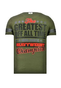 Olivgroen T-shirt met tekst "The Greatest Off All Time Local Fanatic Heavyweight Champion" in zwart, grijs en rood, met sterren en strepen op de mouwen.