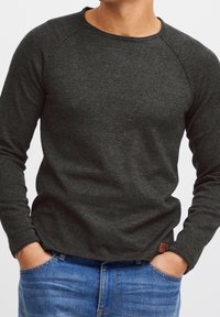 Pull gris foncé à manches longues avec un col rond, tissu texturé et manches raglan. Présente une petite étiquette de la marque près de l'ourlet.