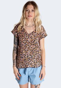 Haut à motifs floraux avec une base noire, doté de manches courtes et d'un décolleté en V. Fabriqué en tissu léger, associé à un short bleu clair.