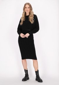 Maglione nero lavorato a maglia, cropped, con un pattern testurizzato e maniche lunghe, abbinato a una gonna midi nera aderente e stivaletti neri.