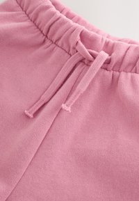 Primer plano de pantalones de chándal rosas que muestran tela tejida, cintura elástica y cordón atado.