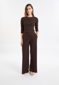 Braunes, geripptes Langarmstrickoberteil mit rundem Ausschnitt und seitlichem Knopfdetail, kombiniert mit braunen, weiten Hosen mit Taschen.