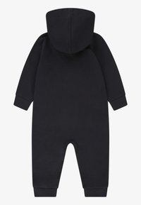 Svart bomulls jumpsuit med hette, lange ermer, elastiske mansjetter og rund bunnåpning for enkel påkledning. Jevn tekstur, minimalistisk design.
