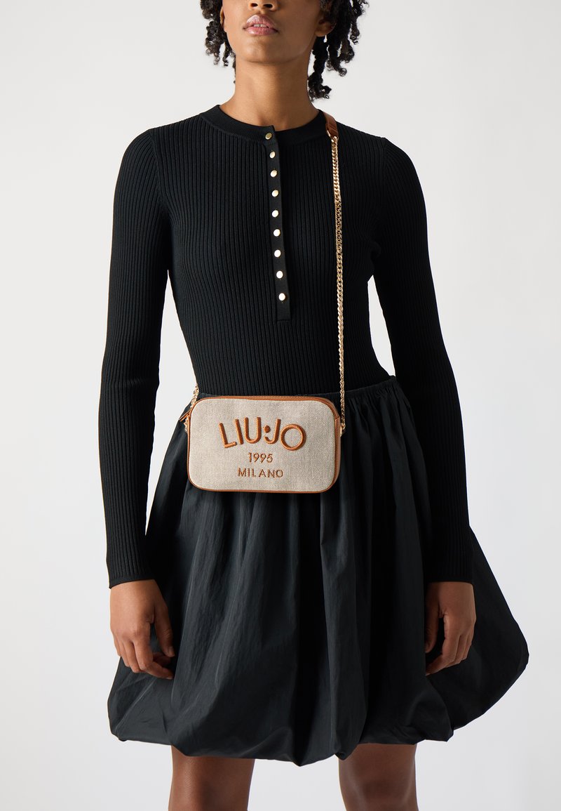 Tamnasti crossbody s torbom s izvezenim natpisom "LIU JO 1995 MILANO" u narančastoj boji, zlatnim lančićem za nošenje i bež tkaninom. Crna rebrasta majica dugih rukava i suknja.