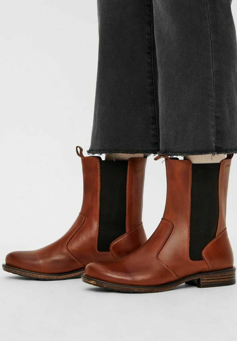 Brune læder Chelsea støvler med sorte elastiske sidepaneler båret med sorte cropped jeans.