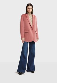 Blazer de lana rosa con solapas de muesca, un solo botón y dos bolsillos frontales, combinado con un cuello de tortuga texturizado y jeans acampanados.