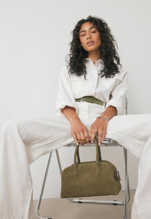Borsa in suede verde oliva con due manici arrotondati, dotata di chiusura a zip e texture liscia, su uno sfondo neutro.