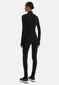 Canotta atletica nera con collo alto e maniche lunghe, abbinata a leggings aderenti coordinati. Il materiale sembra liscio ed elastico.