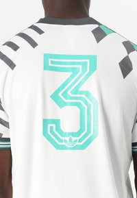 Fehér sportmez, hátán egy nagy türkiz "3"-as számmal, fekete csíkokkal és részletekkel, valamint bordázott gallérral.