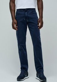 Pantalones de color azul oscuro, con cintura elástica y cordón, cinco bolsillos y corte ajustado. El material parece suave con un ligero brillo.