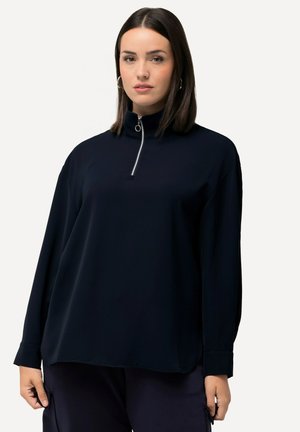 Pull-over bleu marine avec un col montant et fermeture éclair demi-longueur. Manches longues avec une coupe décontractée et texture de tissu lisse.