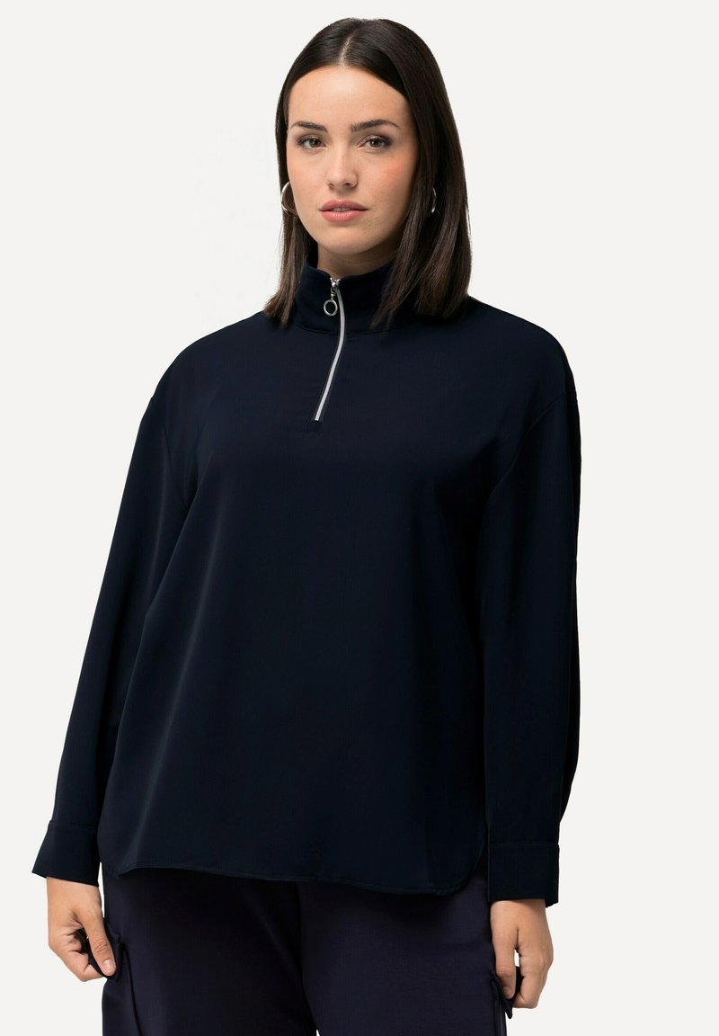 Dunkelblauer Pullover mit hohem Kragen und halbseitigem Reißverschluss. Lange Ärmel mit lockerer Passform und glatter Stoffoberfläche.