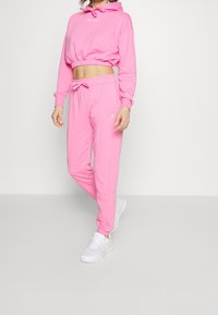 Felpa cropped rosa e pantaloni della tuta abbinati, entrambi realizzati in tessuto morbido. Presentano un logo sul davanti, un cordoncino in vita e polsini elasticizzati.