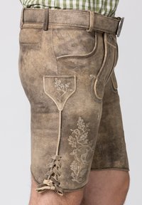 Bruine leren lederhosen met geborduurde bloemenpatronen en een zijstrikaccent. Voorzien van zakken en een getailleerd ontwerp.