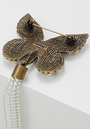 Broche en bronze en forme de papillon avec motif texturé, fermoir à épingle et brins suspendus de petites perles blanches attachés en bas.