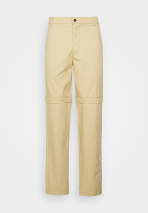 Beige, rechtlopende broek met een knoopsluiting, voorzien van een naad voor een oprol-transformatie en bedrukte tekst langs het linkerbeen.