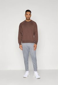 Hnedá mikina, sivé tepláky a biele tenisky; mäkká tkanina, rebrované manžety a lem; neformálny športový vzhľad s jednoduchým dizajnom.