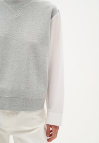 Felpa grigia con finitura testurizzata, dotata di scollatura a V, orlo a coste e maniche lunghe di camicia bianca che spuntano da sotto.