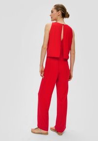 Roter Jumpsuit mit ärmellosem Design, offenem Rücken mit Knopfverschluss, weitem Bein und einem glatten, leichten Stoff.