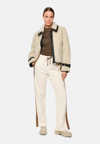 Faux shearling jacket in cream with black trim, paired with a leopard print top and cream pants with brown side stripes. Chunky beige sneakers.