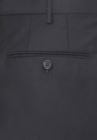 Tessuto grigio scuro con una tasca welt sul retro e una chiusura con bottone nero singolo su pantaloni su misura.