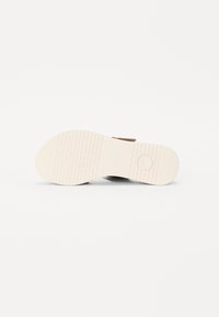 Brown sandal with a textured leather upper, featuring a white rubber sole with traction patterns and a circular accent near the heel.
