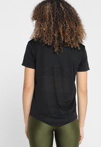 Svart träningströja med korta ärmar, med en nätpanel på baksidan och rundad nederkant, i kombination med olivgröna leggings.