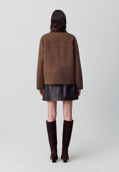 Veste en mélange de laine marron avec une coupe décontractée et un col replié, associée à une mini-jupe en cuir noir et des bottes en suède marron jusqu'au genou.