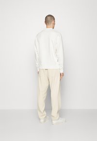 Felpa in cotone bianca con scollo rotondo, abbinata a pantaloni beige a gamba larga. L'outfit è completato da sneakers bianche.