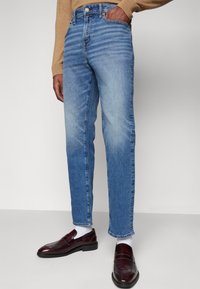 Lys blå denimjeans med lett falming, rett snitt, fem lommer og knappelukking, kombinert med mørke loafers og hvite sokker.