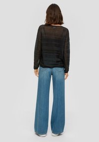 Top nero trasparente a maniche lunghe con righe orizzontali abbinato a jeans in denim blu a gamba larga. Dettagli notevoli includono una vestibilità oversize e orlo grezzo.