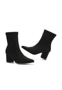 Botines negros de tobillo hechos de tela suave, con punta afilada, tacón cuadrado y un diseño ajustado sin cremalleras ni cierres visibles.