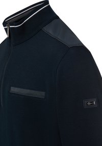 Granatowy sweter z zamkiem do połowy długości i teksturowanej tkaniny, kontrastującym kołnierzem oraz syntetycznymi wstawkami na ramionach. Posiada kieszeń na piersi z detalem ze skóry.