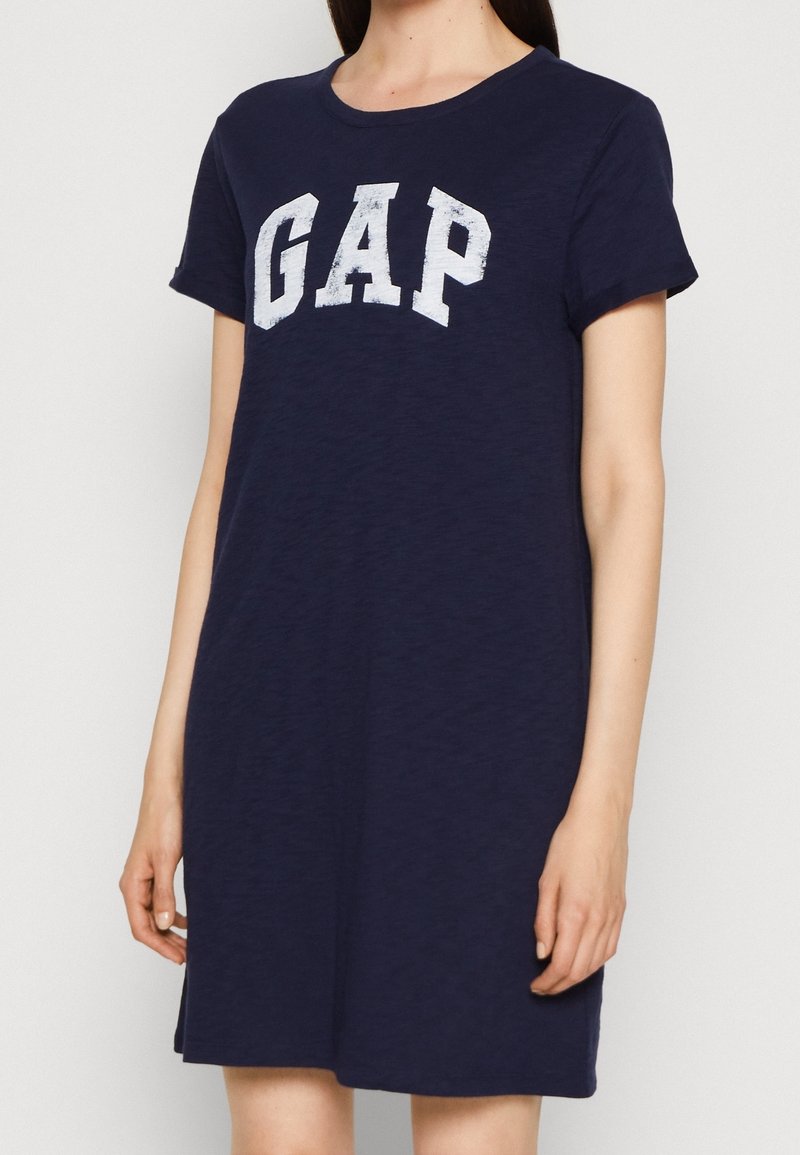 Femme portant une robe bleu marine à manches courtes avec le logo blanc GAP imprimé sur la poitrine.
